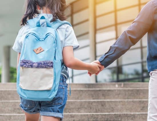 Back to school education concept with girl kid (elementary student) carrying backpacks holding parent woman or mother's hand walking up school building stair going to class