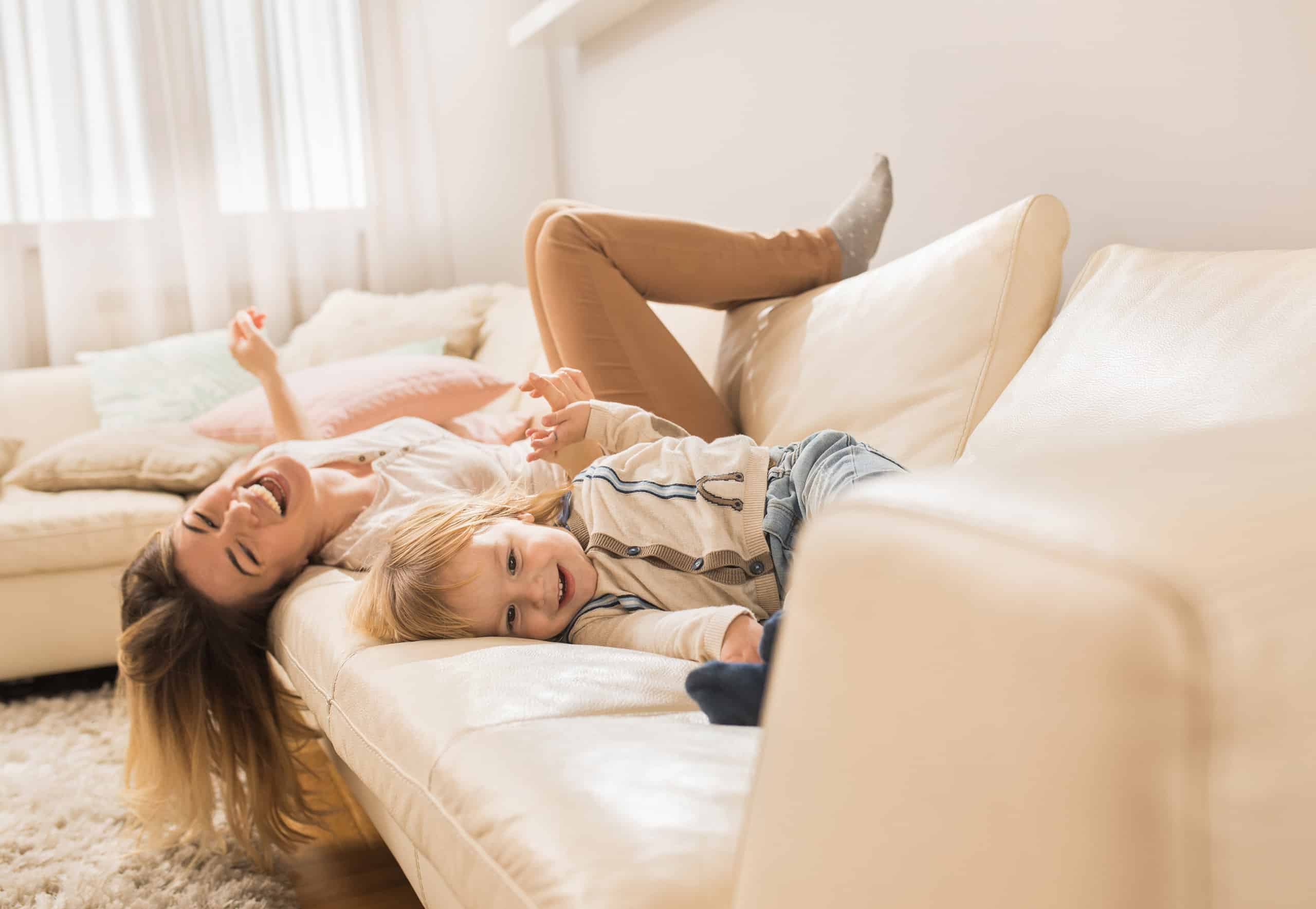 Nanny playing and laughing with a young child on a couch, reflecting the warm in home care Trusting Connections provides