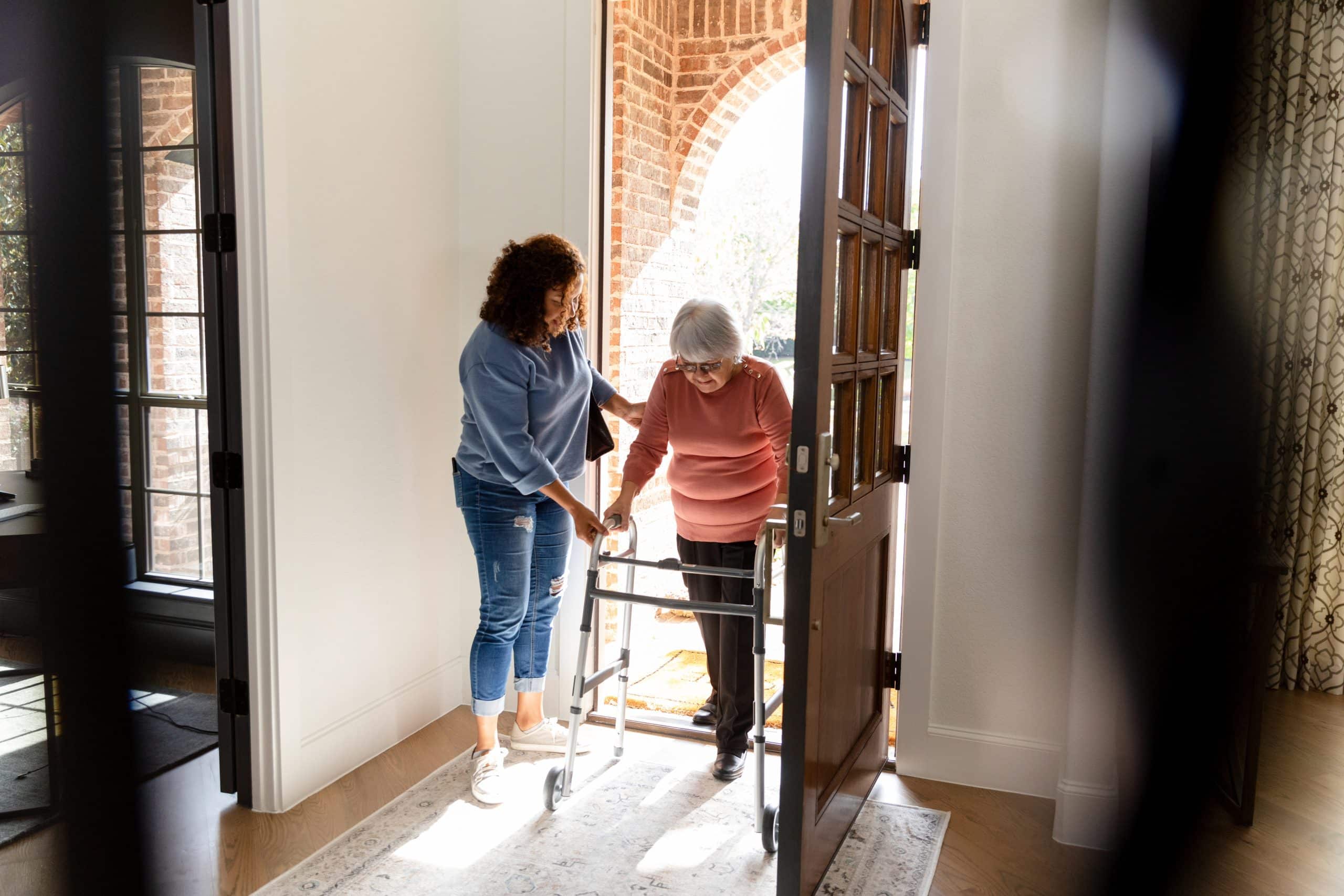 Caregiver assisting senior with walker at doorway for specialized care