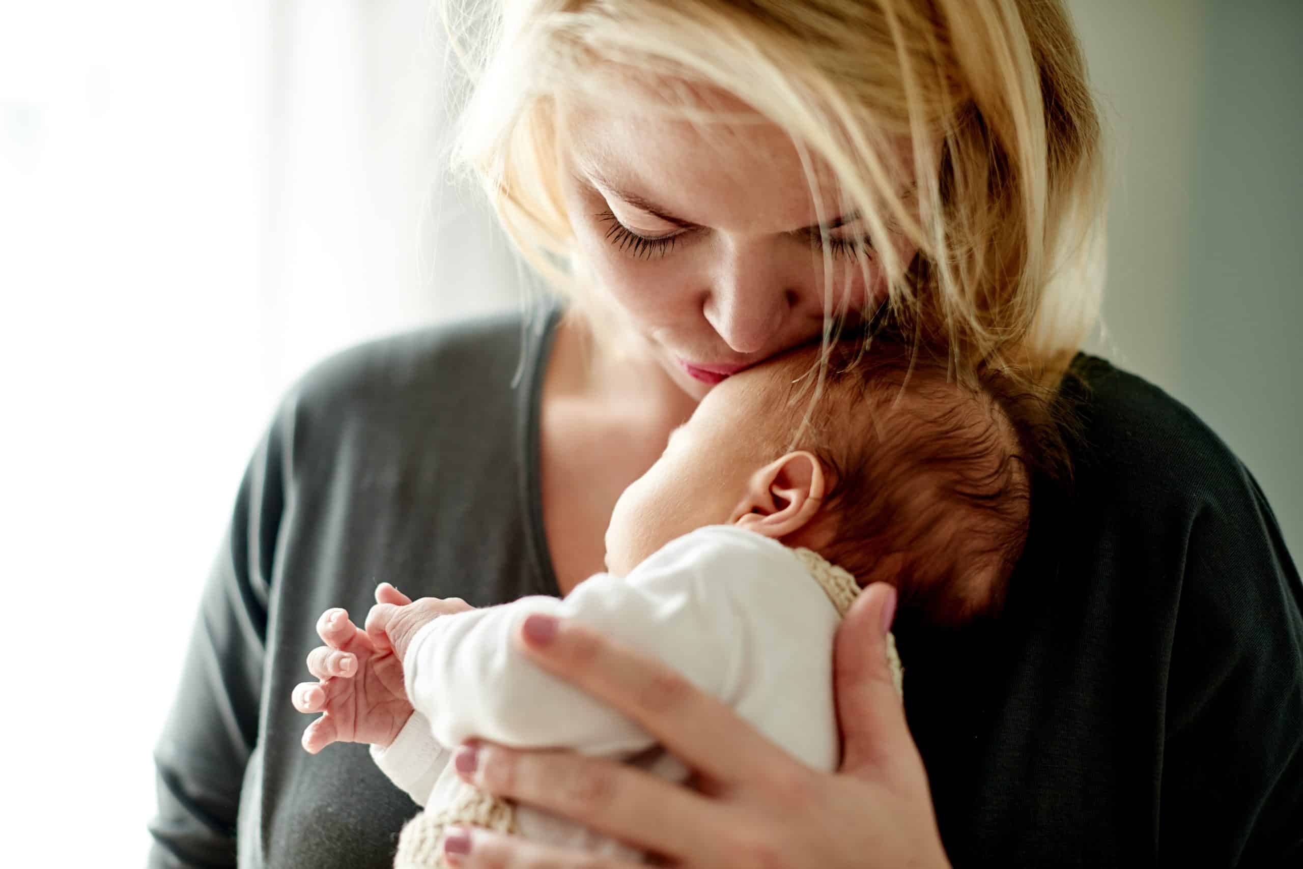 Caregiver kissing a newborn's head while cradling them close, the standard behind every hire