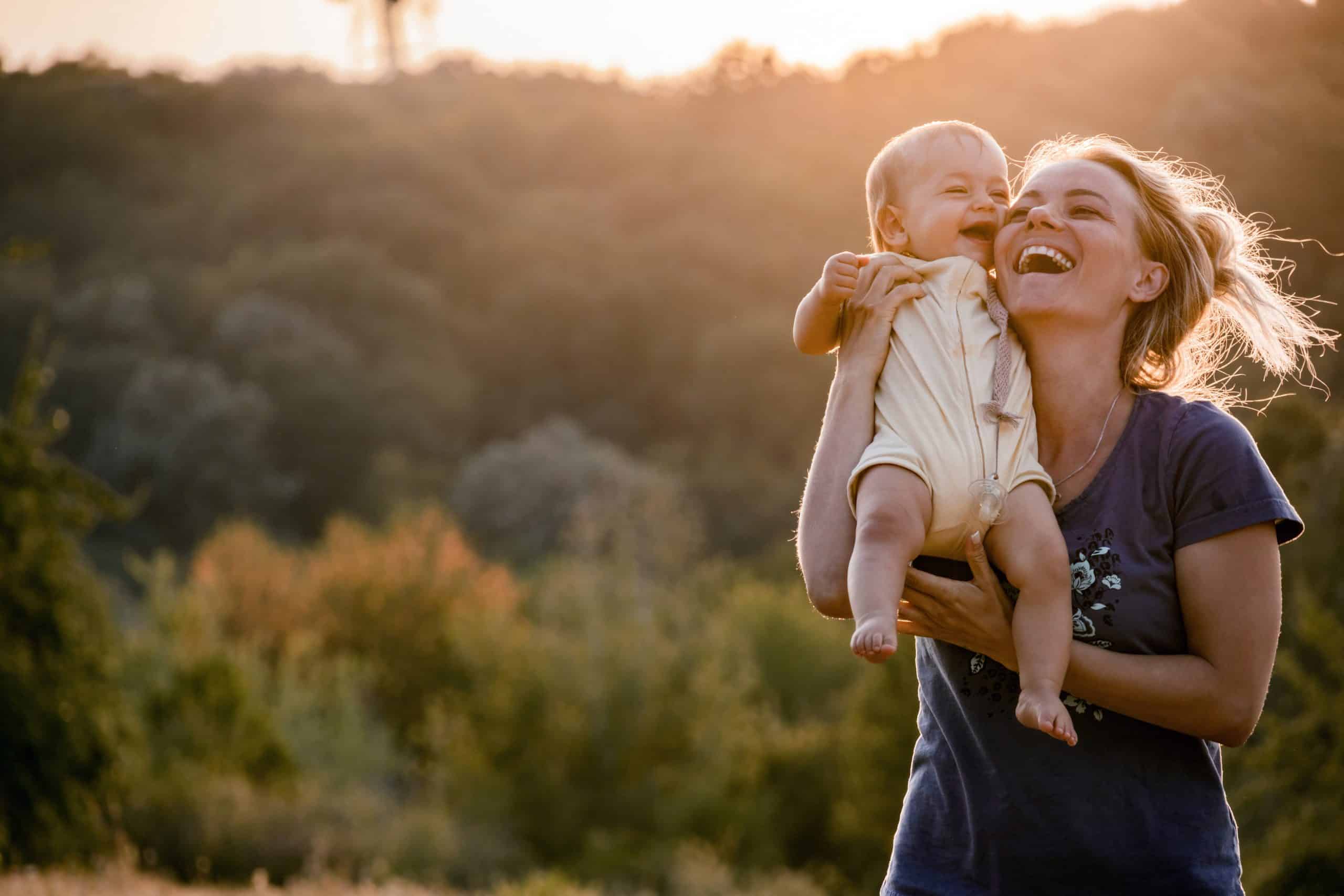 Caregiver laughing joyfully with a baby at golden hour, the joy of caregiving as a career