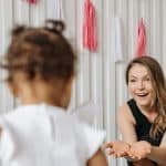 Caregiver reaching out with open hands toward a child by a decorated crib, welcoming them in from day one