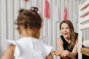 Caregiver reaching out with open hands toward a child by a decorated crib, welcoming them in from day one