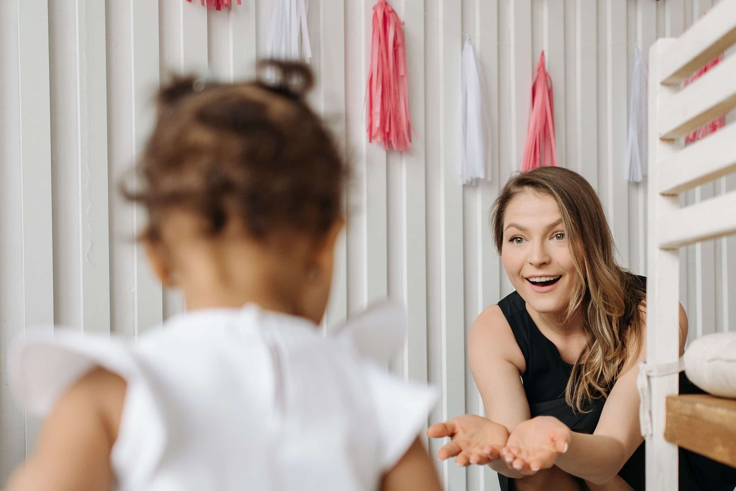 Caregiver reaching out with open hands toward a child by a decorated crib, welcoming them in from day one