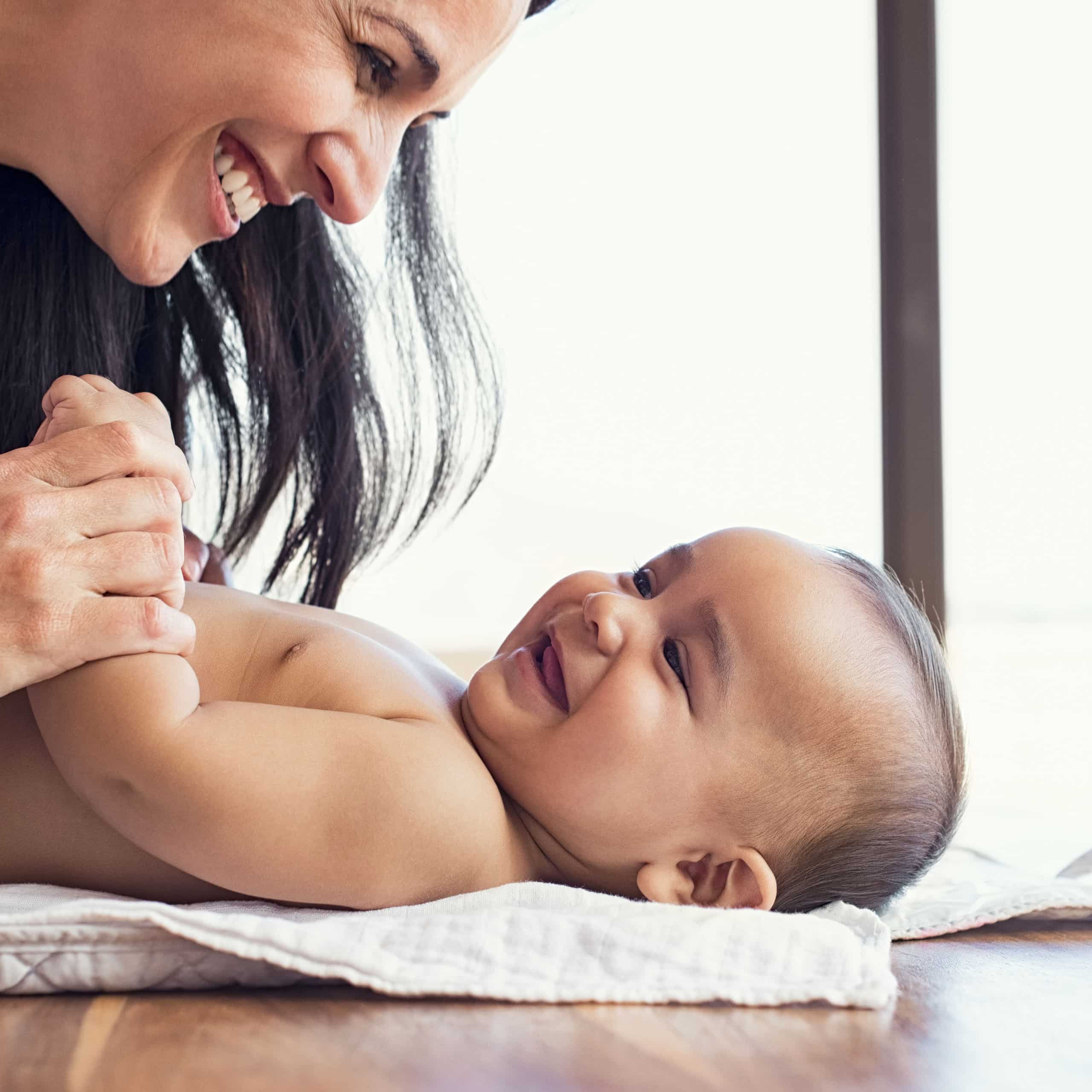 Caregiver smiling at a giggling baby during diaper change, trusted babysitting care