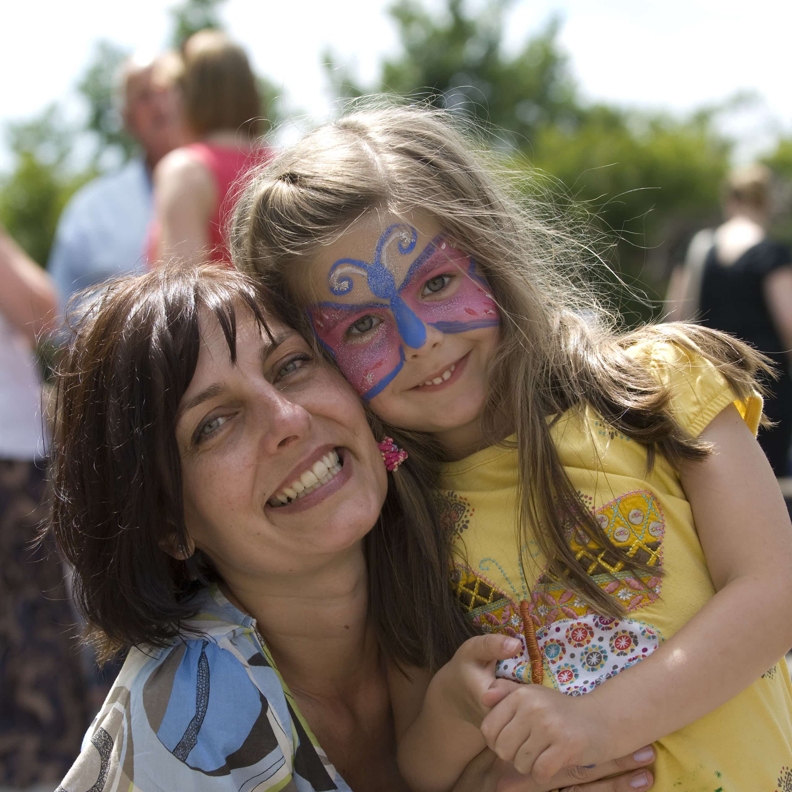 Caregiver smiling with a girl in butterfly face paint, event childcare families can fully enjoy
