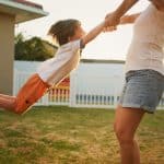 Caregiver swinging a joyful boy by the hands at golden hour, standards proven in everyday moments