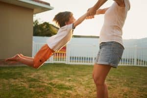 Caregiver swinging a joyful boy by the hands at golden hour, standards proven in everyday moments