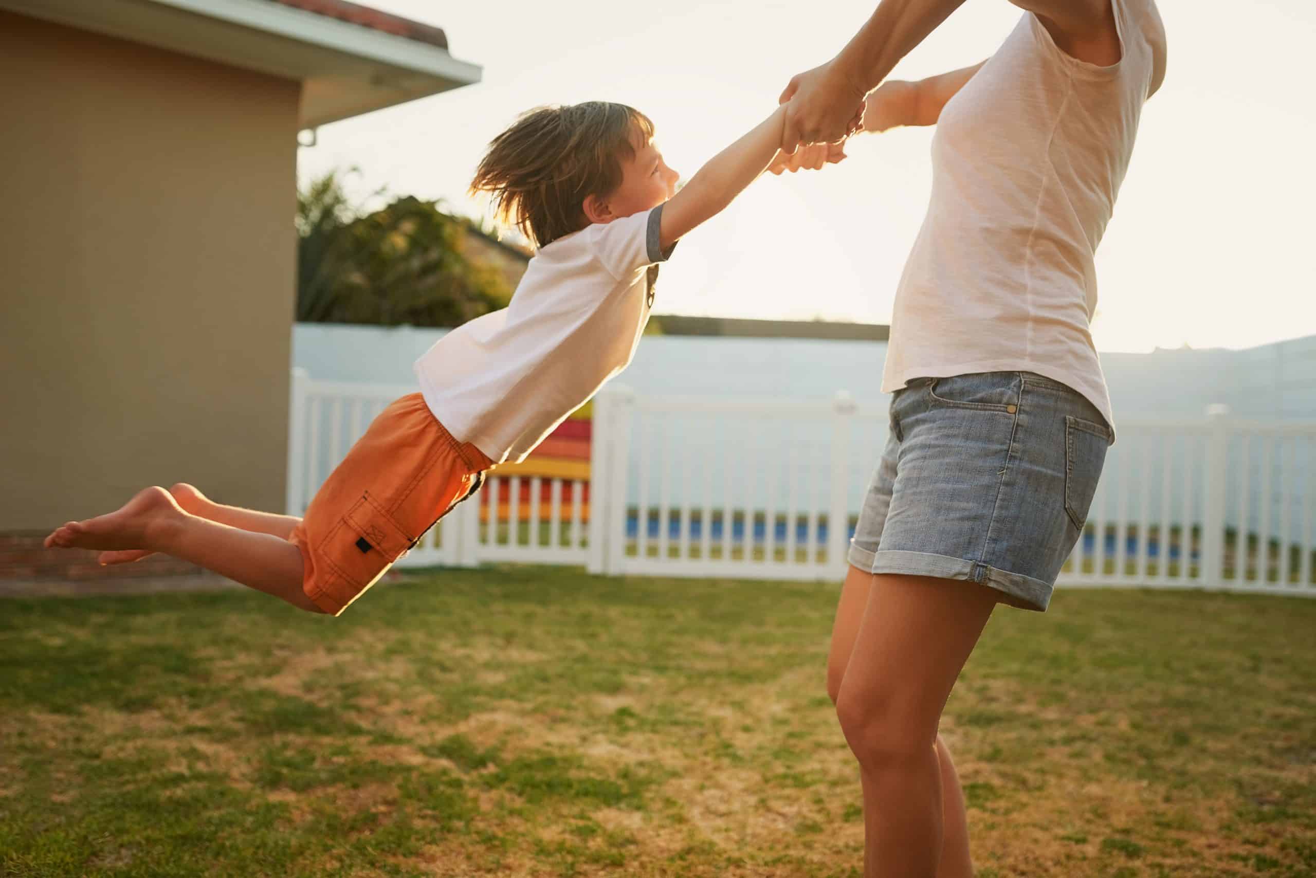 Caregiver swinging a joyful boy by the hands at golden hour, standards proven in everyday moments
