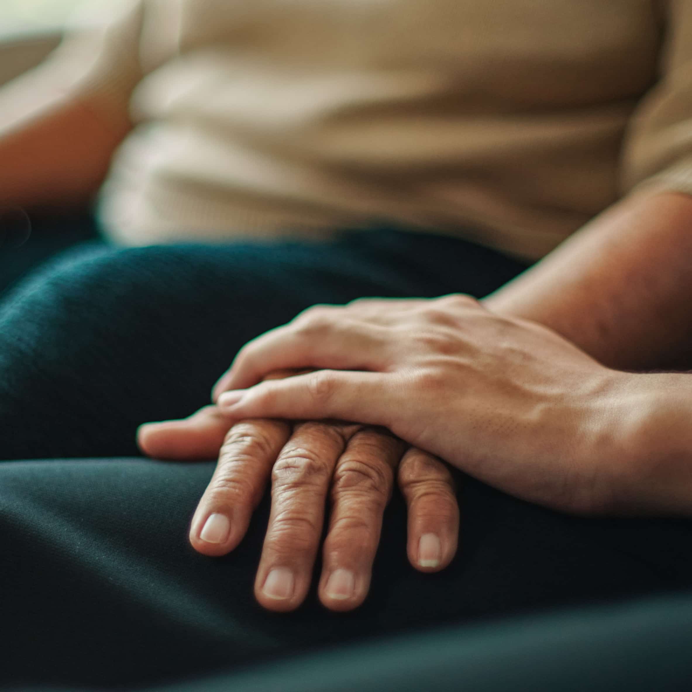 Caregiver's hand resting gently over senior's hands, comfort in every act of care