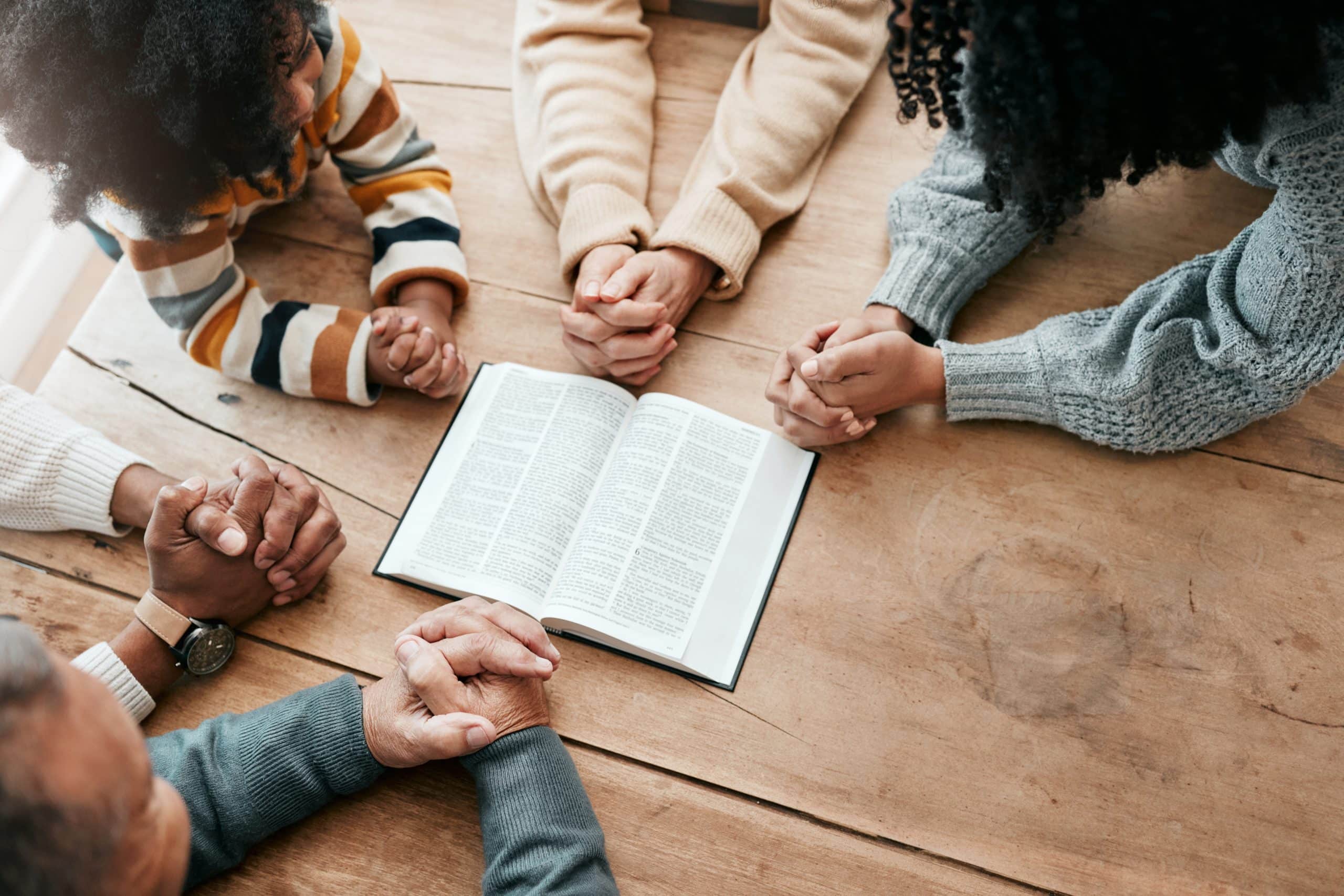 Hands joined in prayer around an open Bible, fully managed childcare support for churches