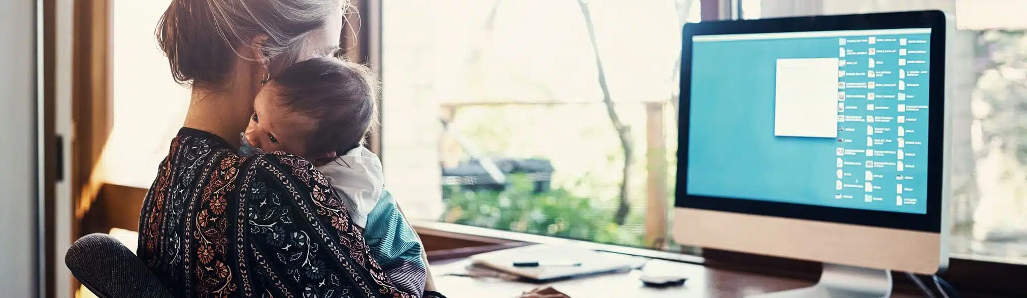 Mom juggling work and childcare at her desk, the disruption back up childcare programs solve