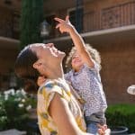 Nanny holding a laughing toddler pointing up at a courtyard fountain in Dallas Fort Worth