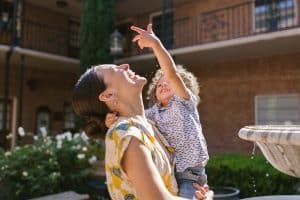 Nanny holding a laughing toddler pointing up at a courtyard fountain in Dallas Fort Worth