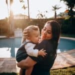 Nanny holding a smiling toddler beside a backyard pool in Phoenix, Arizona