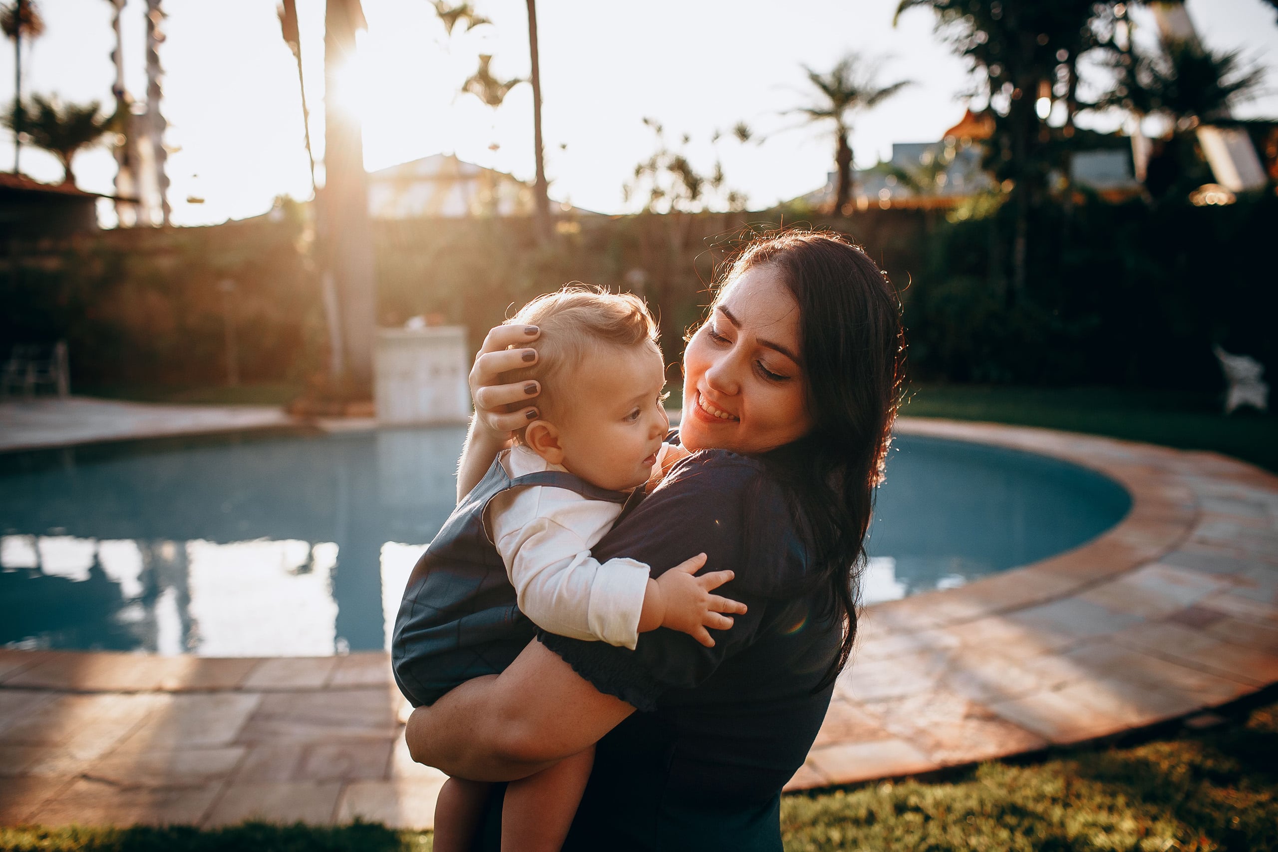 Nanny holding a smiling toddler beside a backyard pool in Phoenix, Arizona