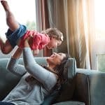 Nanny lifting a giggling baby in the air on the couch, the payoff of thorough DIY screening