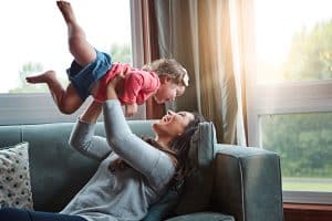 Nanny lifting a giggling baby in the air on the couch, the payoff of thorough DIY screening