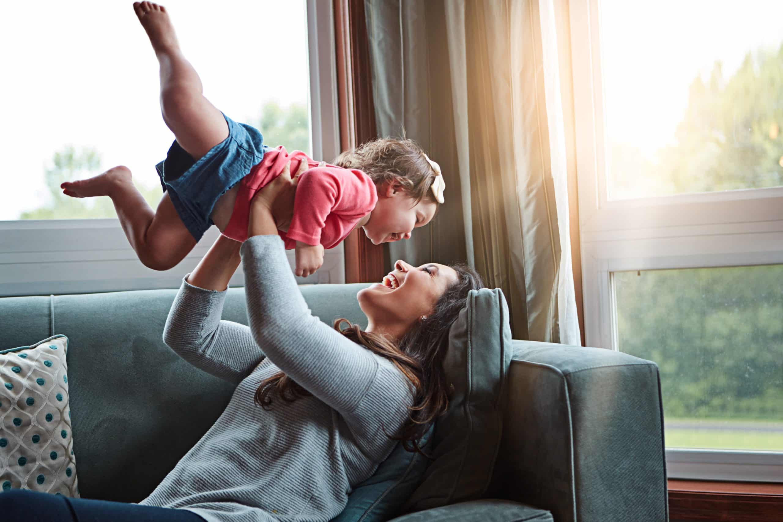 Nanny lifting a giggling baby in the air on the couch, the payoff of thorough DIY screening