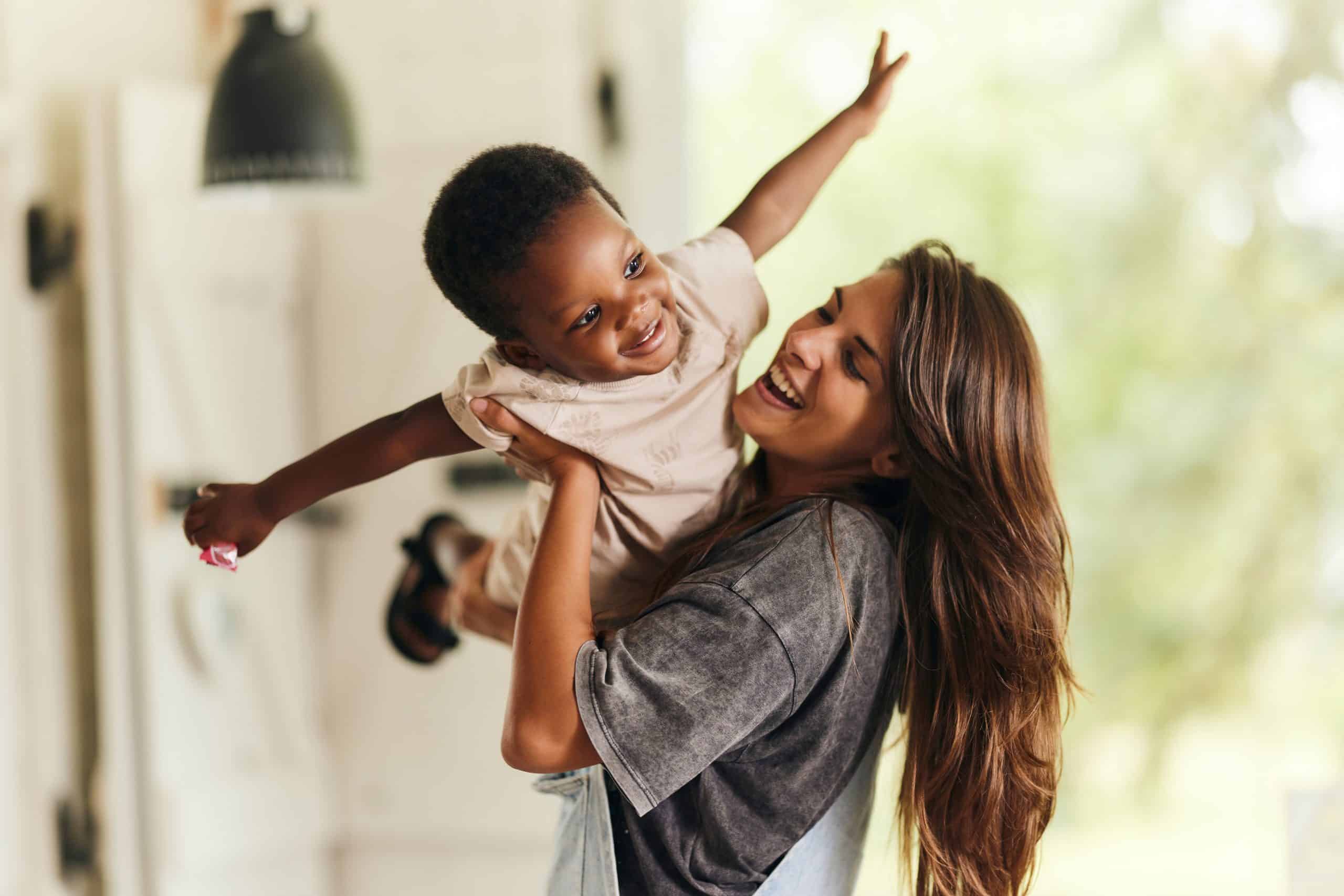 Nanny lifting a joyful toddler overhead, personalized long term nanny placement