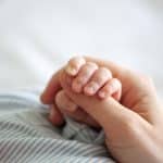 Newborn gently gripping an adult's finger, expert infant care parents can trust
