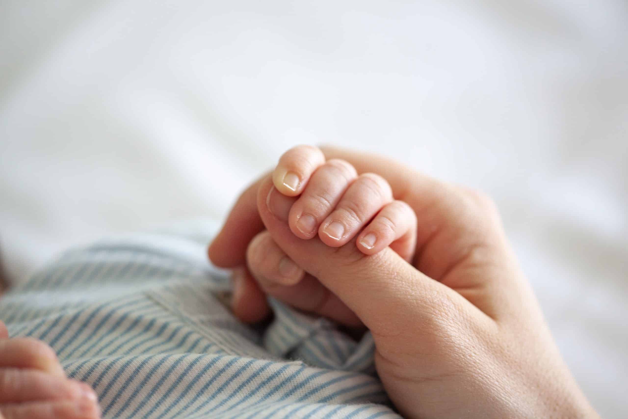 Newborn gently gripping an adult's finger, expert infant care parents can trust