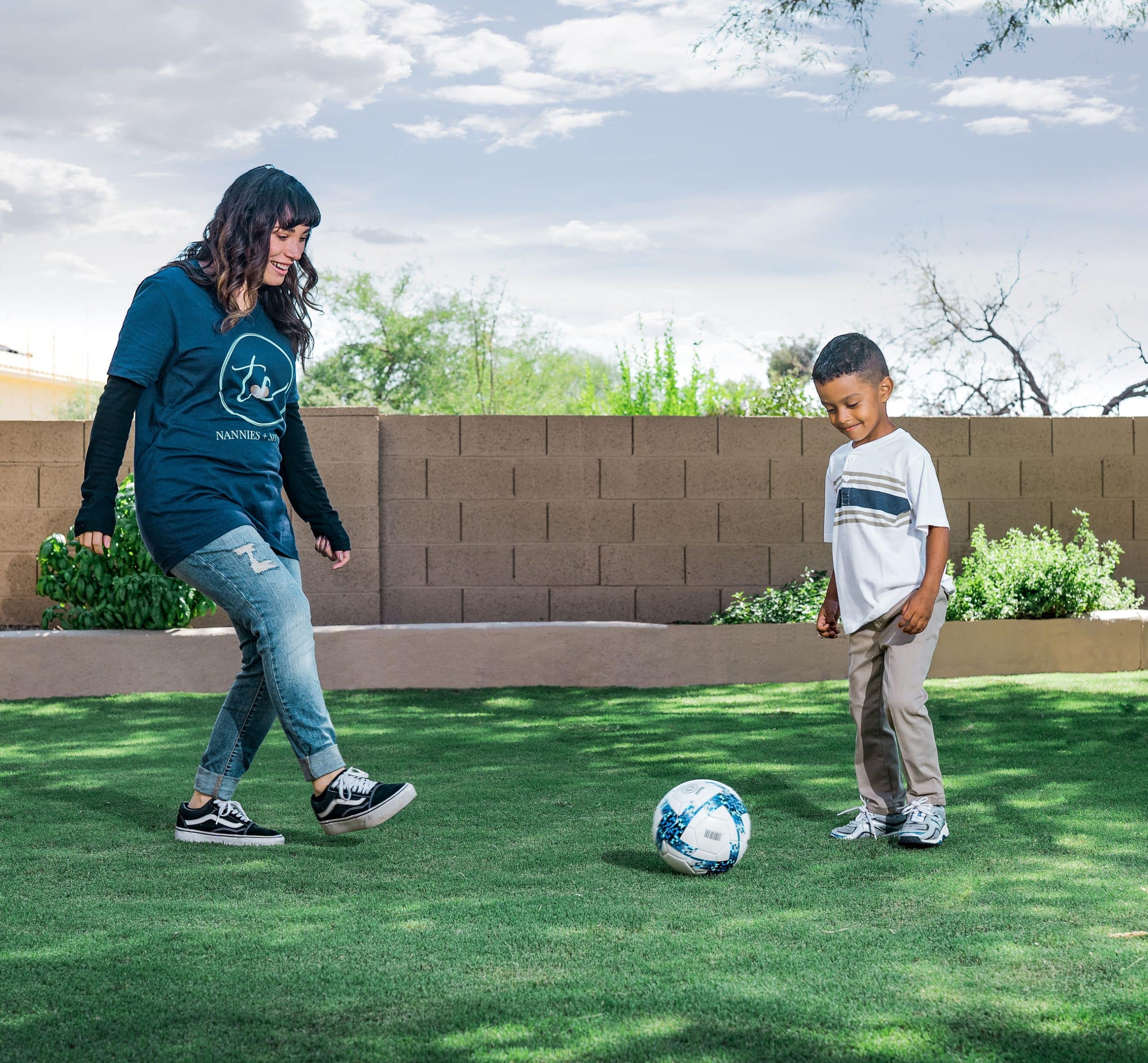 TC nanny playing soccer with young boy in backyard, family care services