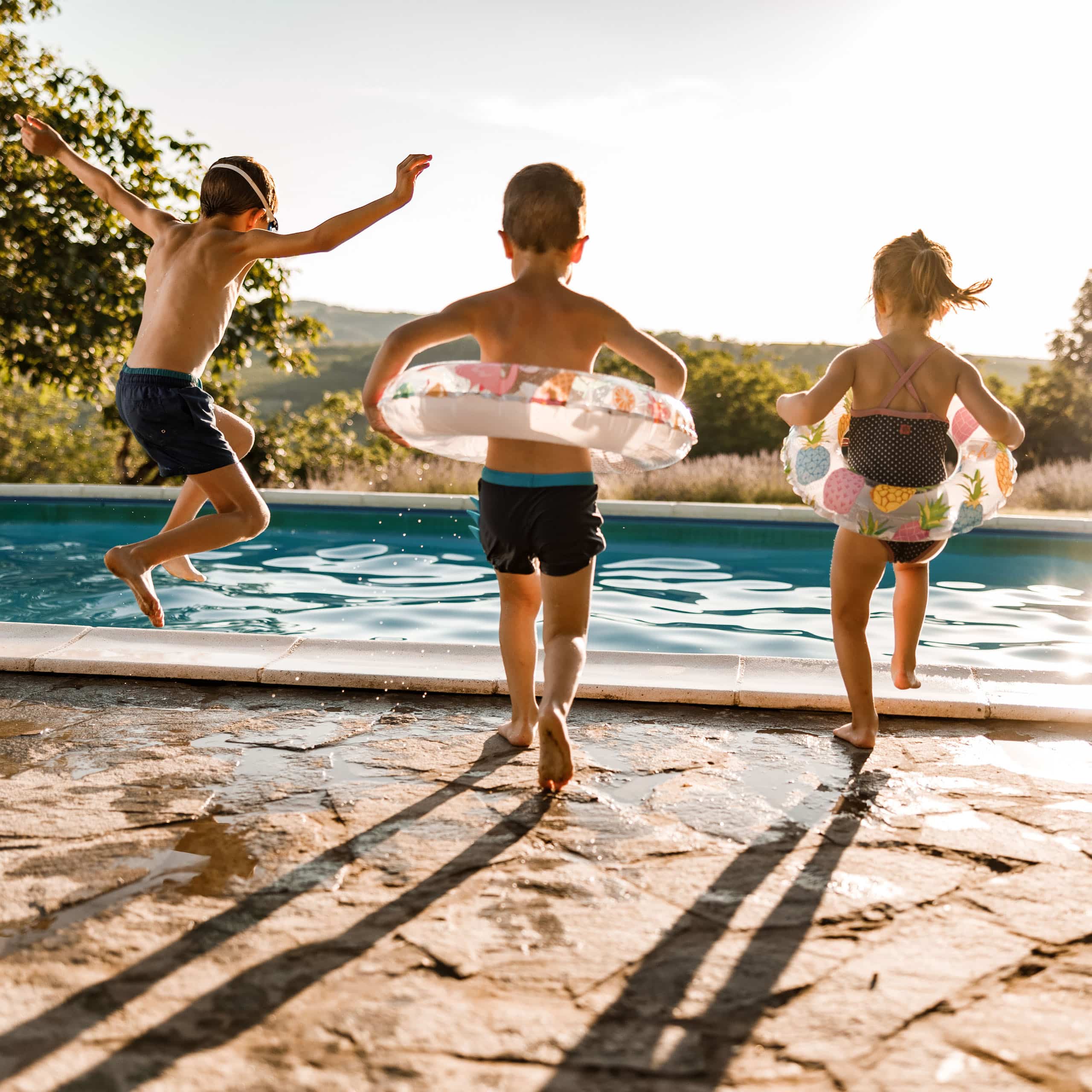 Three kids racing toward the pool at golden hour, the vacation joy trusted care makes possible