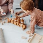 Two caregivers playing with a toddler on wooden toys, considered candidates ready to join our team