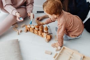 Two caregivers playing with a toddler on wooden toys, considered candidates ready to join our team
