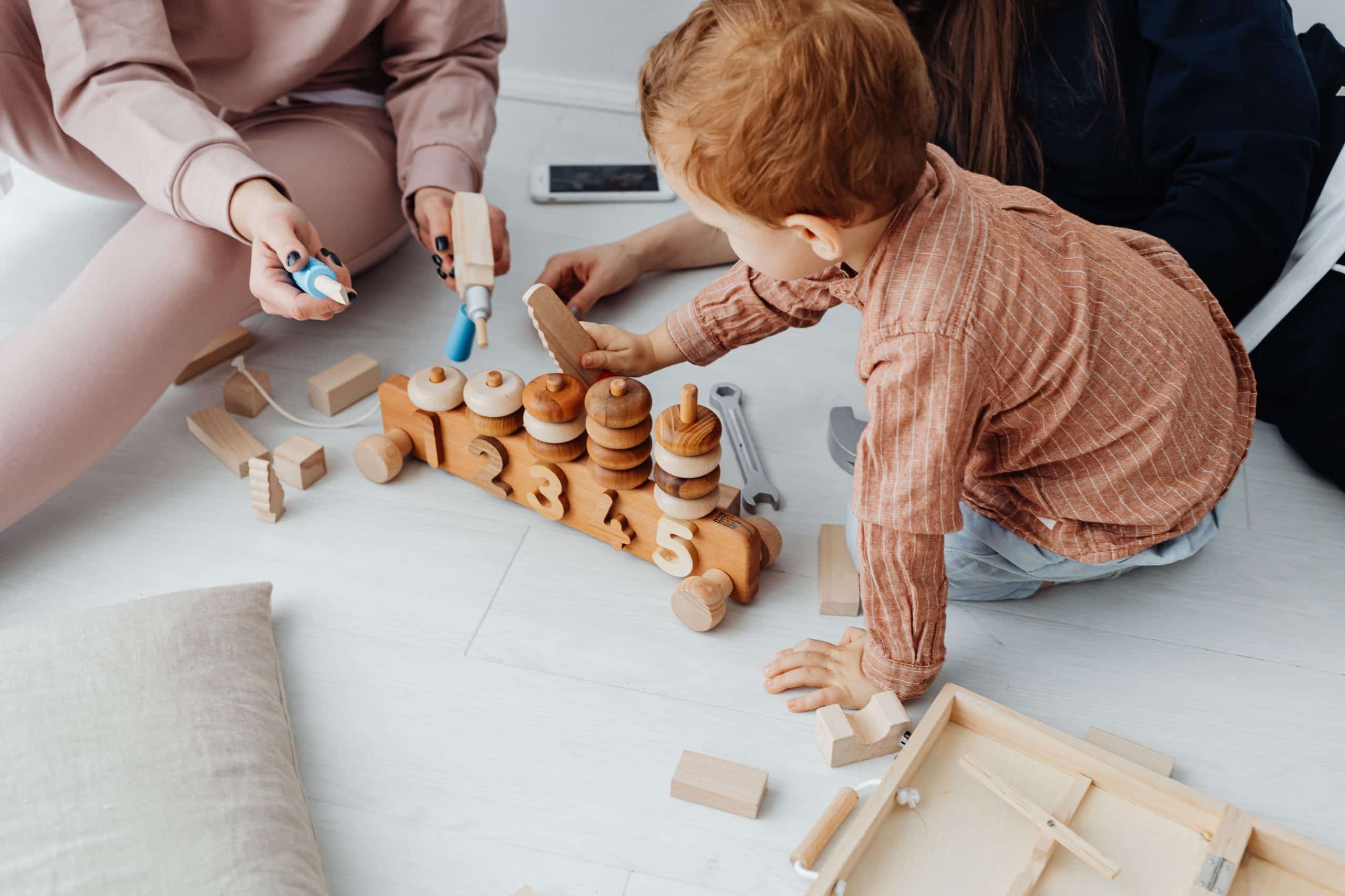 Two caregivers playing with a toddler on wooden toys, considered candidates ready to join our team