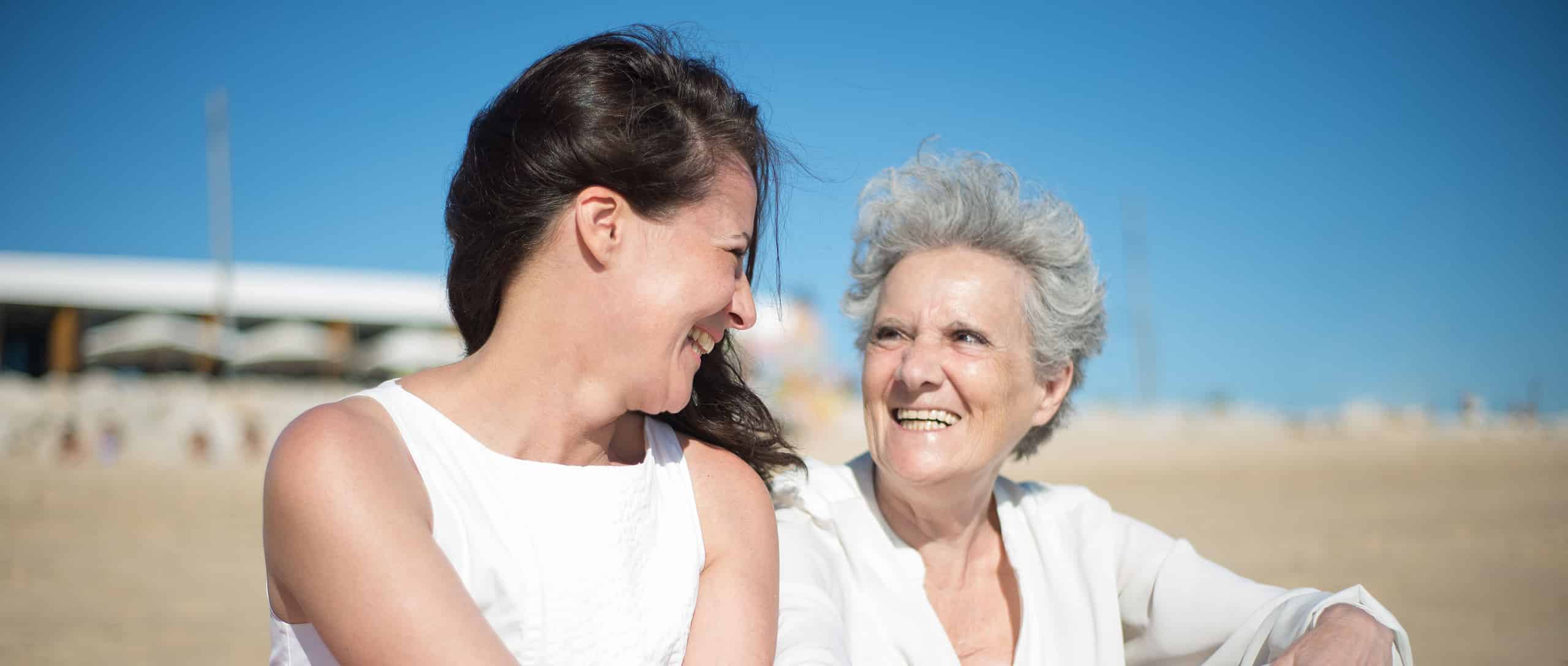 Younger woman and senior laughing together at the beach, compassionate companionship in every visit