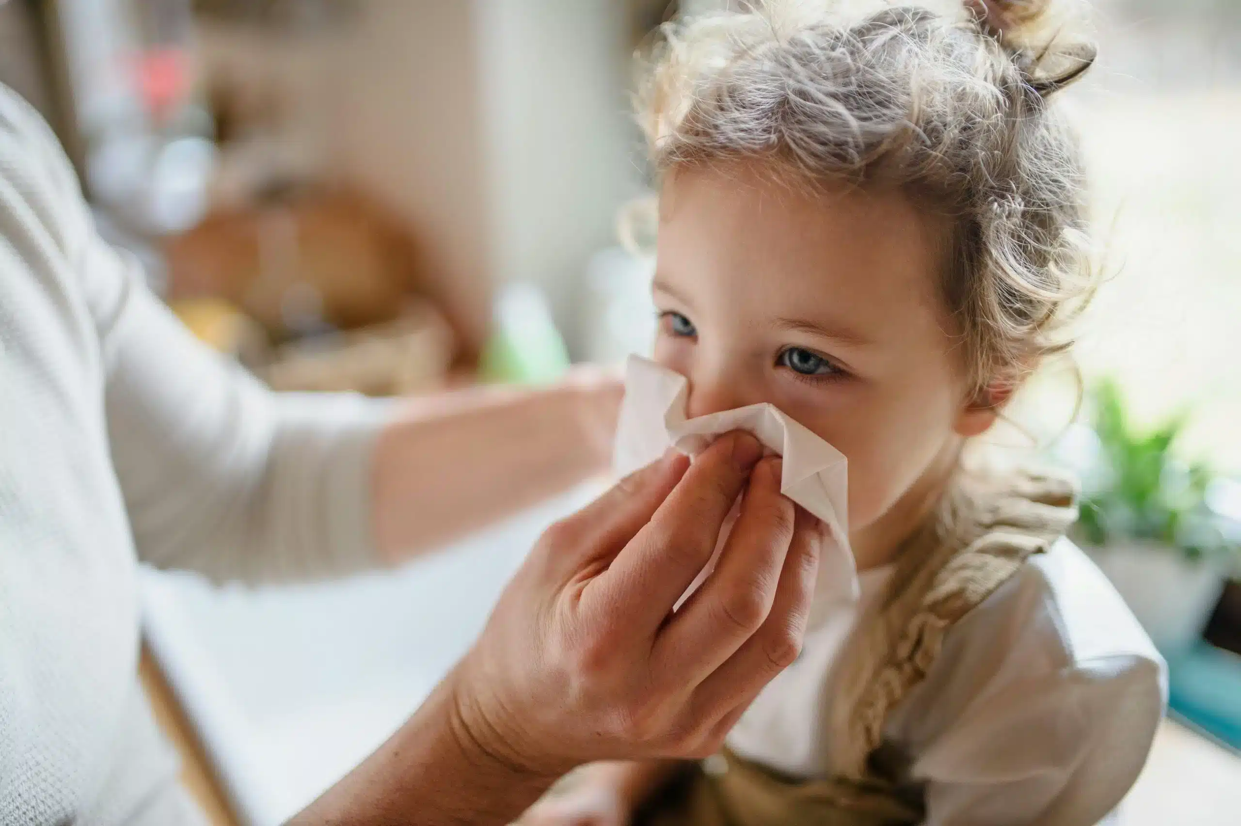 Nanny providing sick child care, gently wiping a toddler's nose during in home care